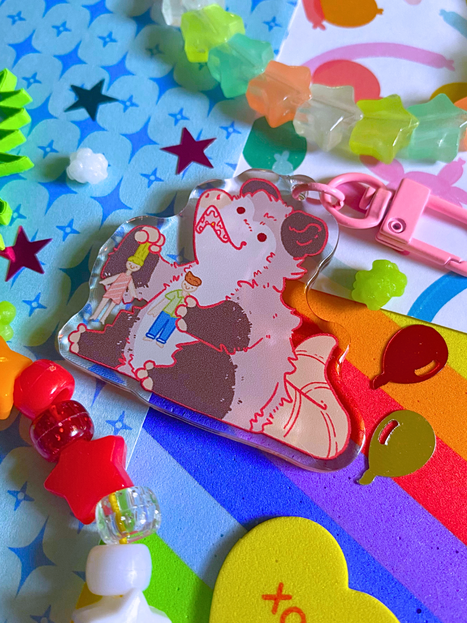 image features one keychain featuring original artwork by candy critters.
details in the background of the product photo contains a collage of printed paper (balloon ani, sparkles, and rainbow), konpeito candy, confetti, and a kandi bracelet. (background items not included in purchase of keychain)
keychain is double sided with same design on both sides. features a drawing of a possum playing with a girl and boy doll.
the hardware for this keychain is pink.