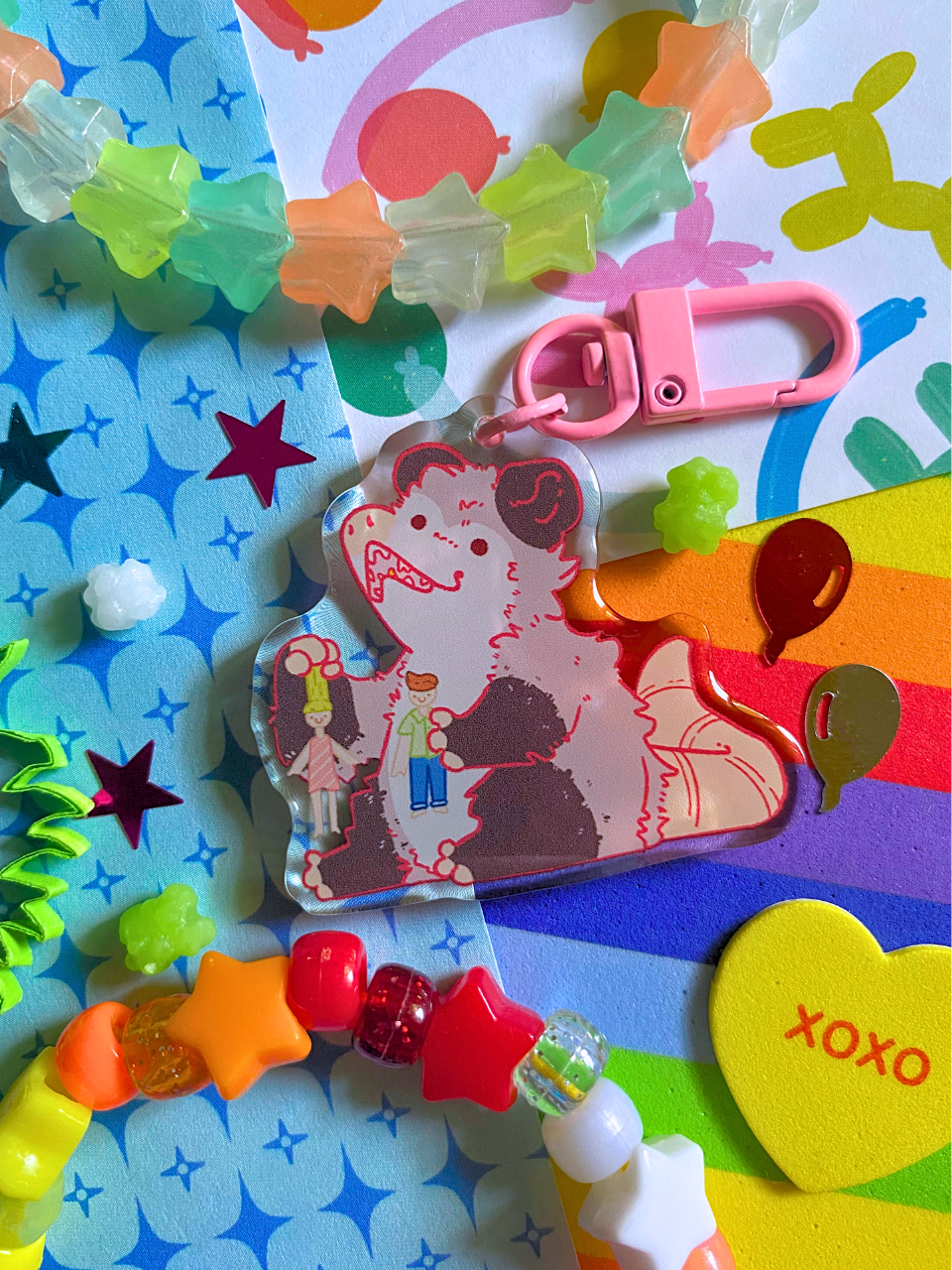 image features one keychain featuring original artwork by candy critters.
details in the background of the product photo contains a collage of printed paper (balloon ani, sparkles, and rainbow), konpeito candy, confetti, and a kandi bracelet. (background items not included in purchase of keychain)
keychain is double sided with same design on both sides. features a drawing of a possum playing with a girl and boy doll.
the hardware for this keychain is pink.