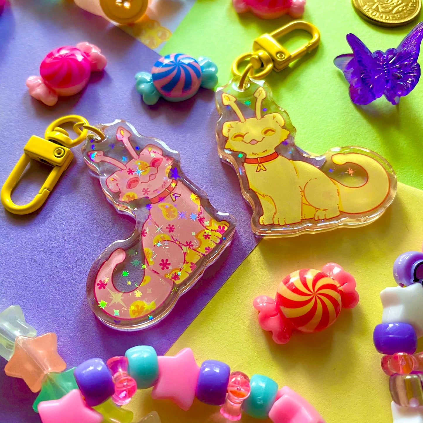 image features two cute keychains featuring original artwork by candy critters. 
details in the background of the product photo contains bracelets, cute hair clips, charms, and an arcade token. (background items not included in purchase of keychain)
left keychain is the front side of the keychain, featuring an aisha (fictional online pet) painted the disco color. 
right keychain is the back side, featuring an aisha painted the yellow color. 
the hardware for this keychain is yellow. 