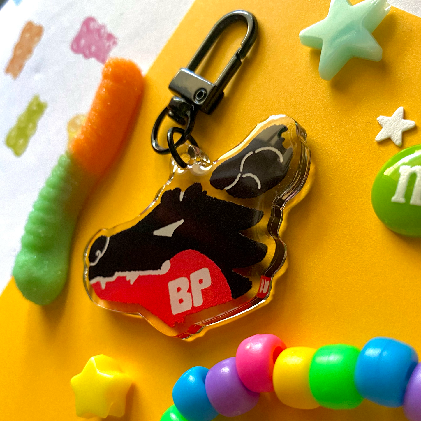 image features one keychain featuring original artwork by candy critters. 
details in the background of the product photo contains a gummy worm, star charms, a candy charm, and a kandi bracelet. (background items not included in purchase of keychain)

 keychain is double sided with the same design on both sides. featuring a drawing of a popular furry fandom brand logo, parodied to be a possum. with the initials BP for "bad possum"
the design is black, red, and white.
the hardware for this keychain is black.