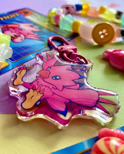 image features one keychain featuring original artwork by candy critters. 
details in the background of the product photo contains a collage of trading cards, candy charms, and a kandi bracelets. (background items not included in purchase of keychain)

 keychain is double sided with same design on both sides. features a drawing of a pink bird with her wings stretched out. 
the hardware for this keychain is pink.