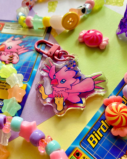 image features one keychain featuring original artwork by candy critters. 
details in the background of the product photo contains a collage of trading cards, candy charms, and a kandi bracelets. (background items not included in purchase of keychain)

 keychain is double sided with same design on both sides. features a drawing of a pink bird with her wings stretched out. 
the hardware for this keychain is pink.