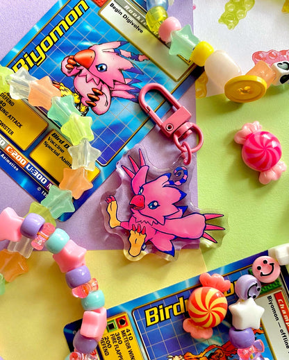 image features one keychain featuring original artwork by candy critters. 
details in the background of the product photo contains a collage of trading cards, candy charms, and a kandi bracelets. (background items not included in purchase of keychain)

 keychain is double sided with same design on both sides. features a drawing of a pink bird with her wings stretched out. 
the hardware for this keychain is pink.