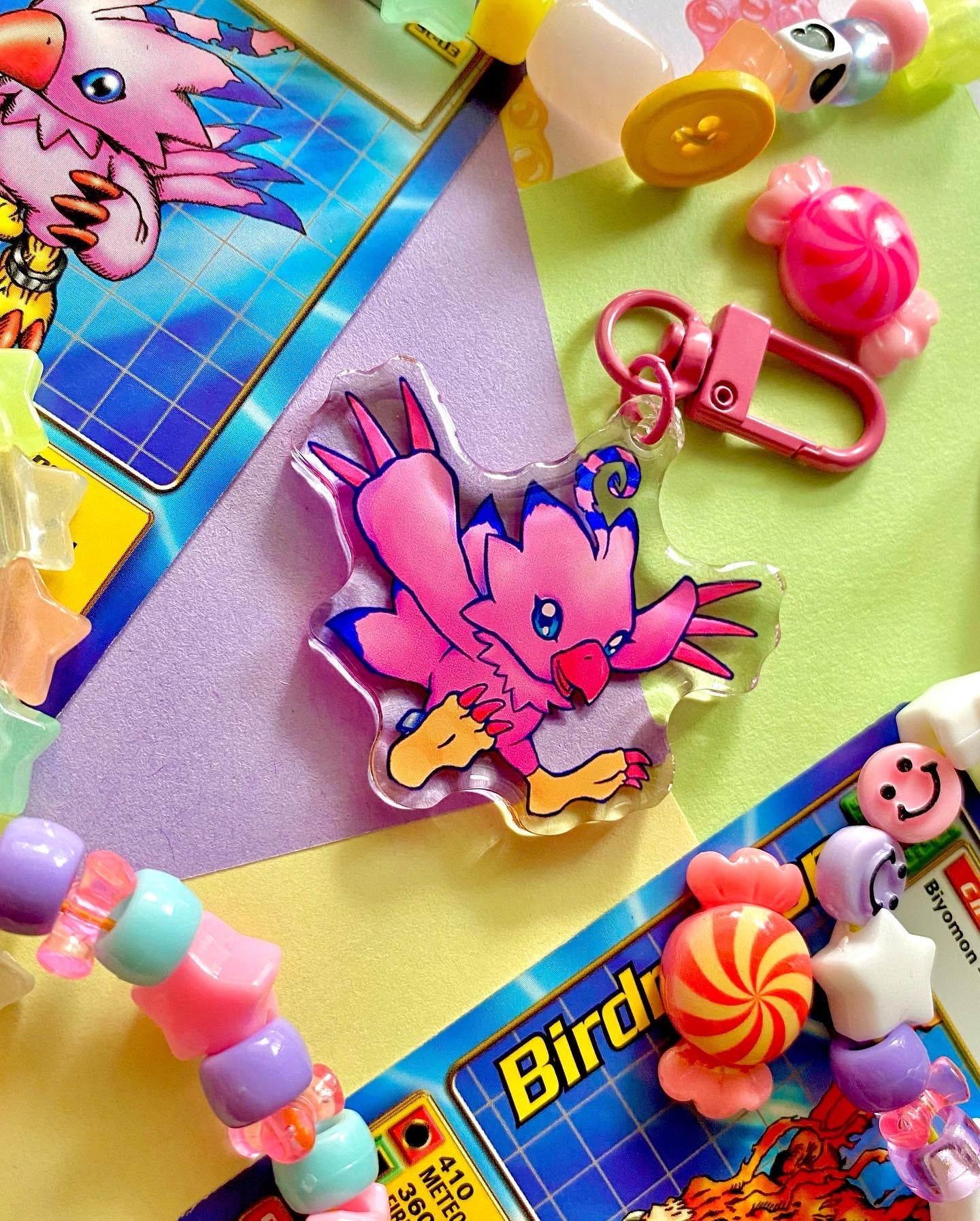 image features one keychain featuring original artwork by candy critters. 
details in the background of the product photo contains a collage of trading cards, candy charms, and a kandi bracelets. (background items not included in purchase of keychain)

 keychain is double sided with same design on both sides. features a drawing of a pink bird with her wings stretched out. 
the hardware for this keychain is pink.