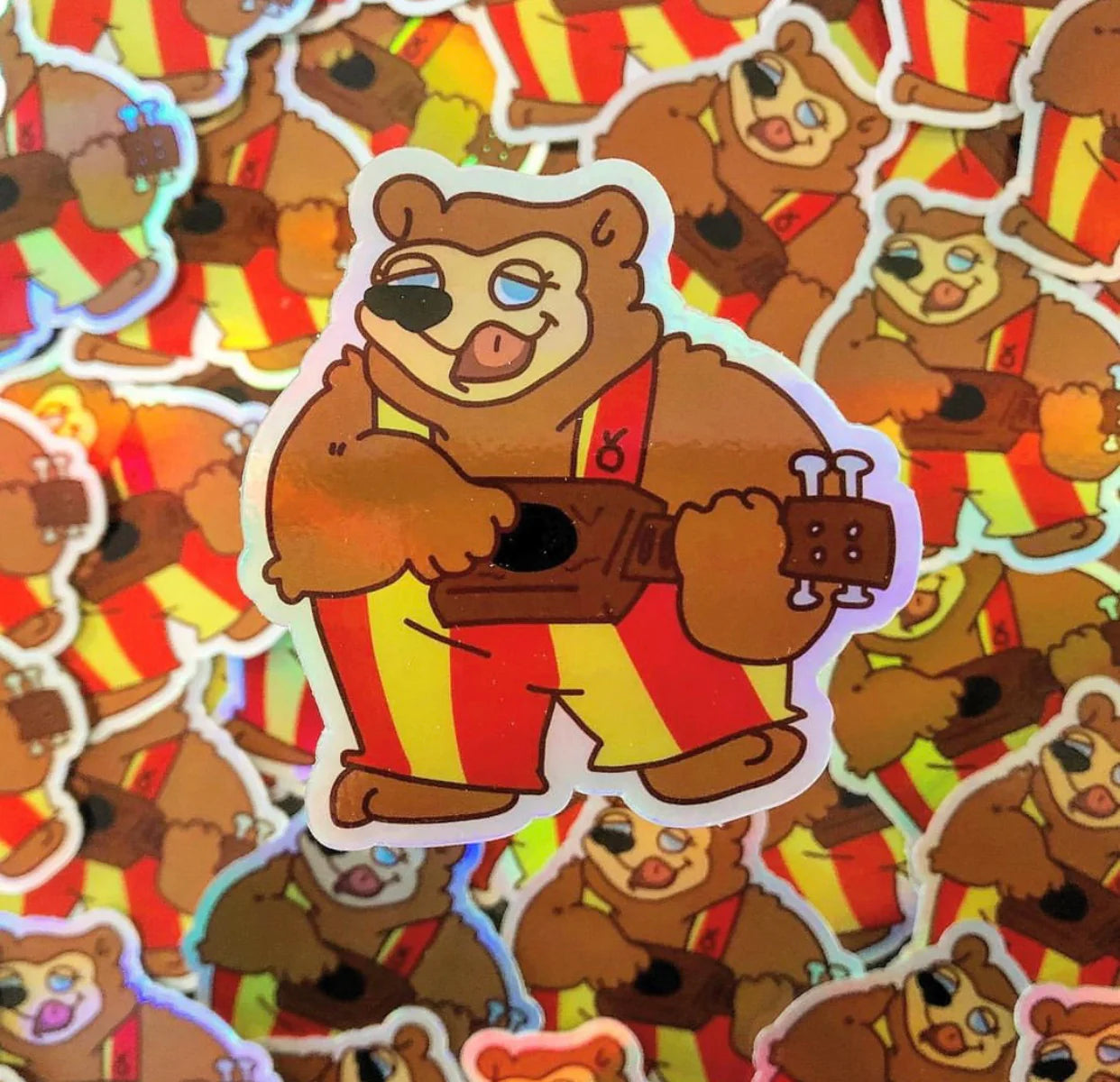 sticker of a bear in striped yellow and red overalls, playing a guitar. 
image background is the sticker overlayed, one sticker is included in purchase,